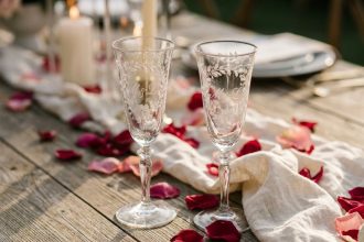 Deux flûtes à champagne gravées avec initiales sur une table en bois rustique décorée de pétales de roses pour un mariage