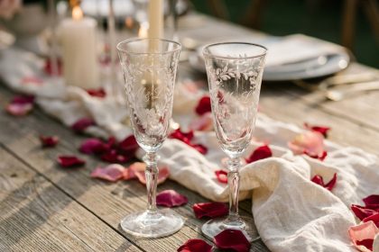 Deux flûtes à champagne gravées avec initiales sur une table en bois rustique décorée de pétales de roses pour un mariage